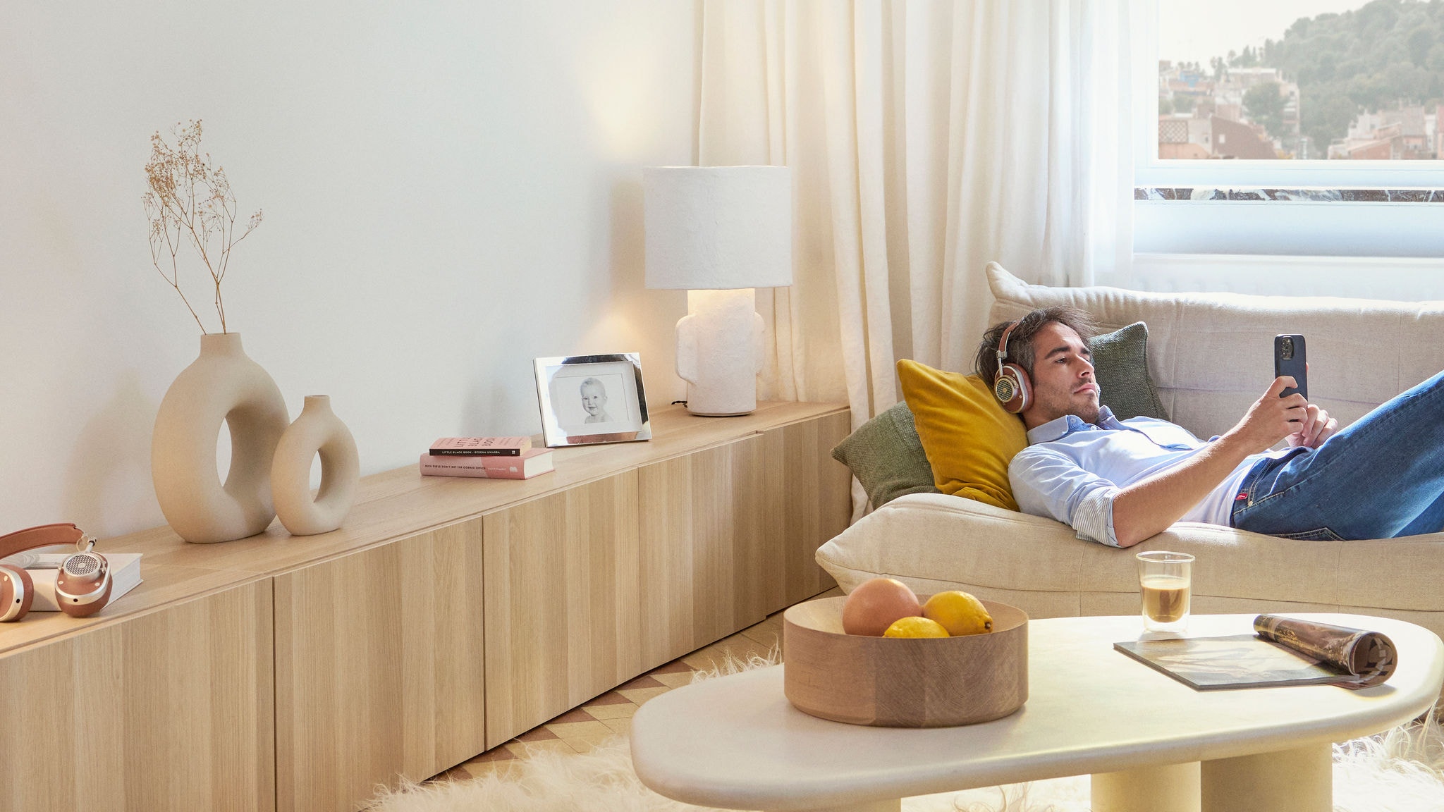 Ontspannen man ligt in de woonkamer op de bank met een hoofdtelefoon op en is bezig op zijn telefoon