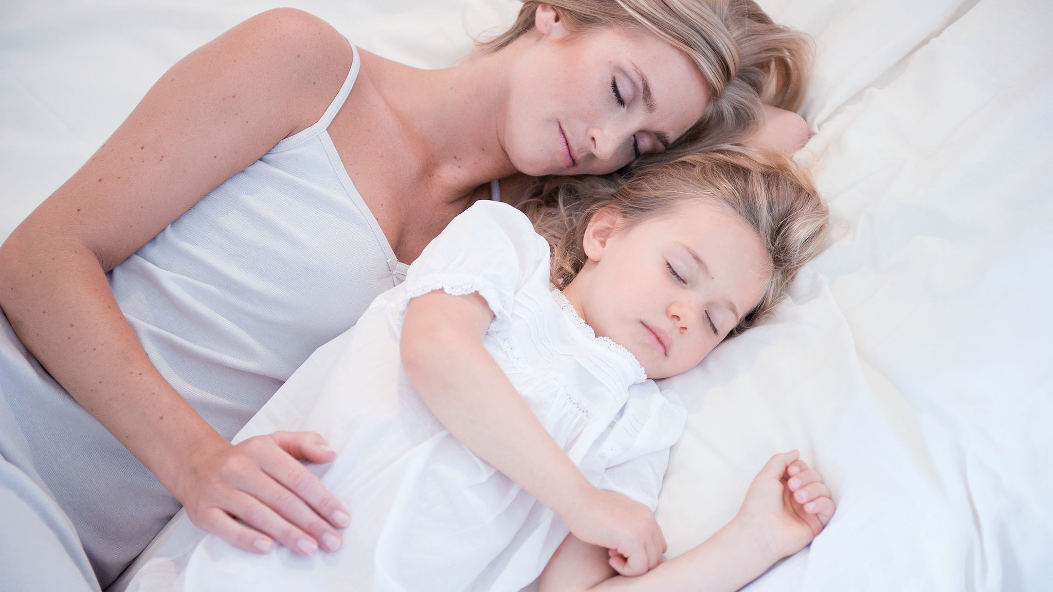 Moeder en dochtertje slapen naast elkaar in een wit bed met zuivere lucht