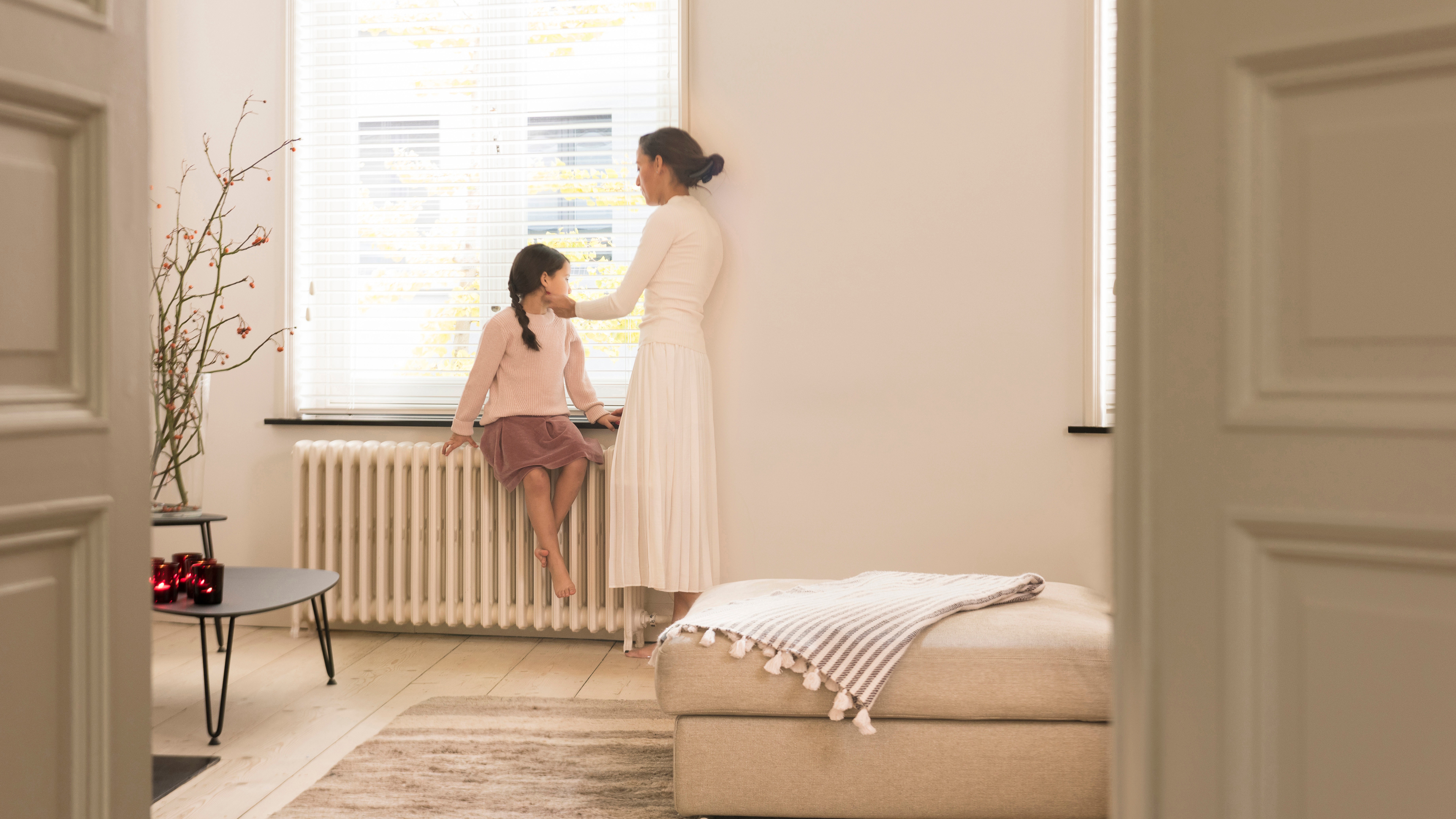 Moeder en dochter kijken uit het raam vanuit hun perfect verwarmde woonkamer