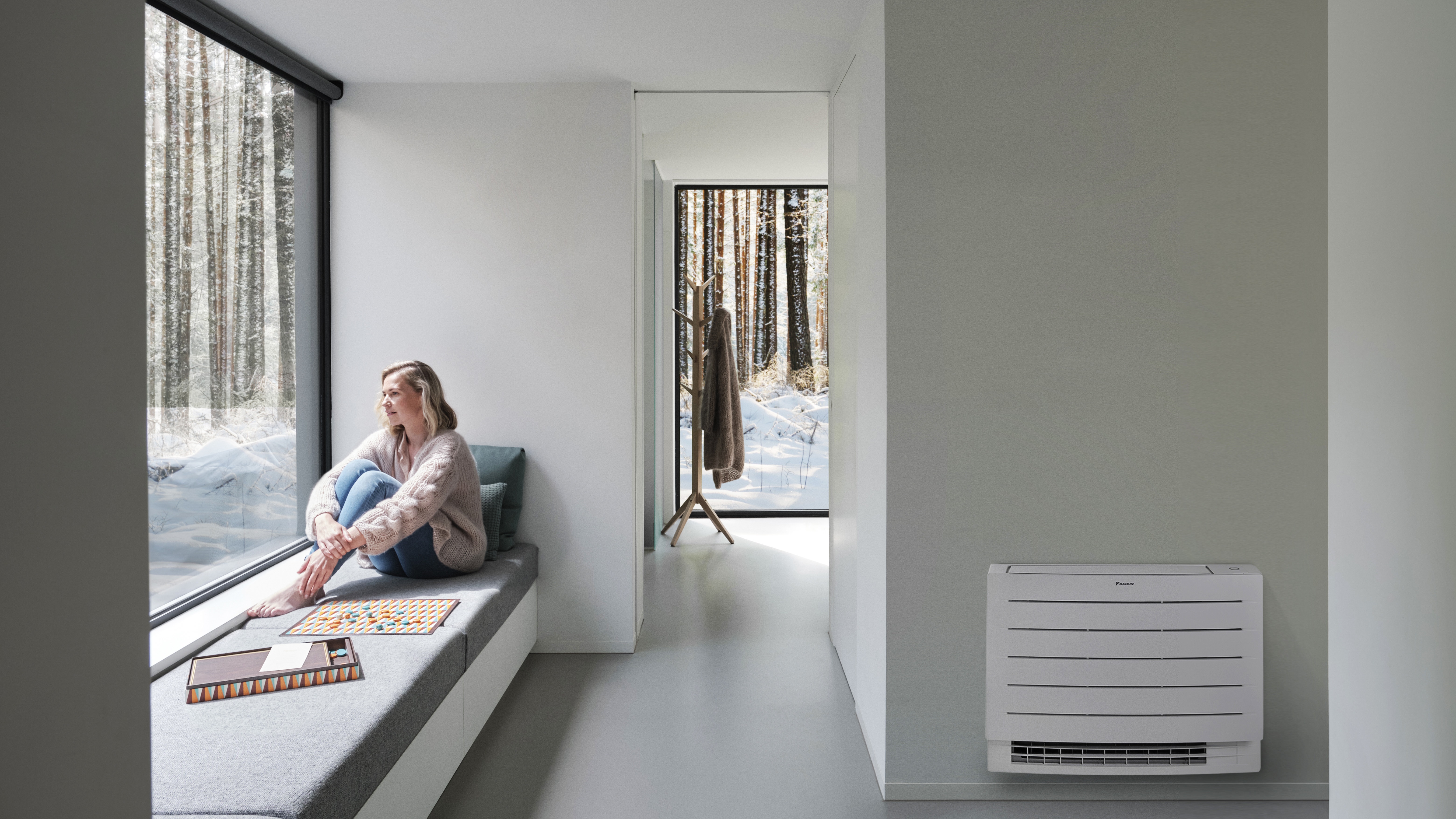 Vrouw kijkt naar de deken sneeuw buiten terwijl ze binnen van een verwarmde woning geniet dankzij het Perfera vloermodel