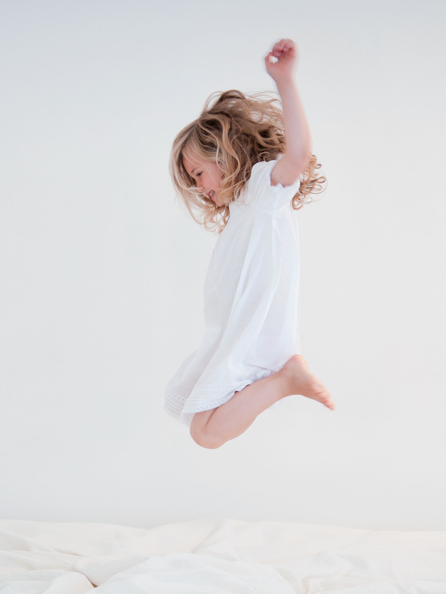 Meisje in witte jurk springt op een wit bed