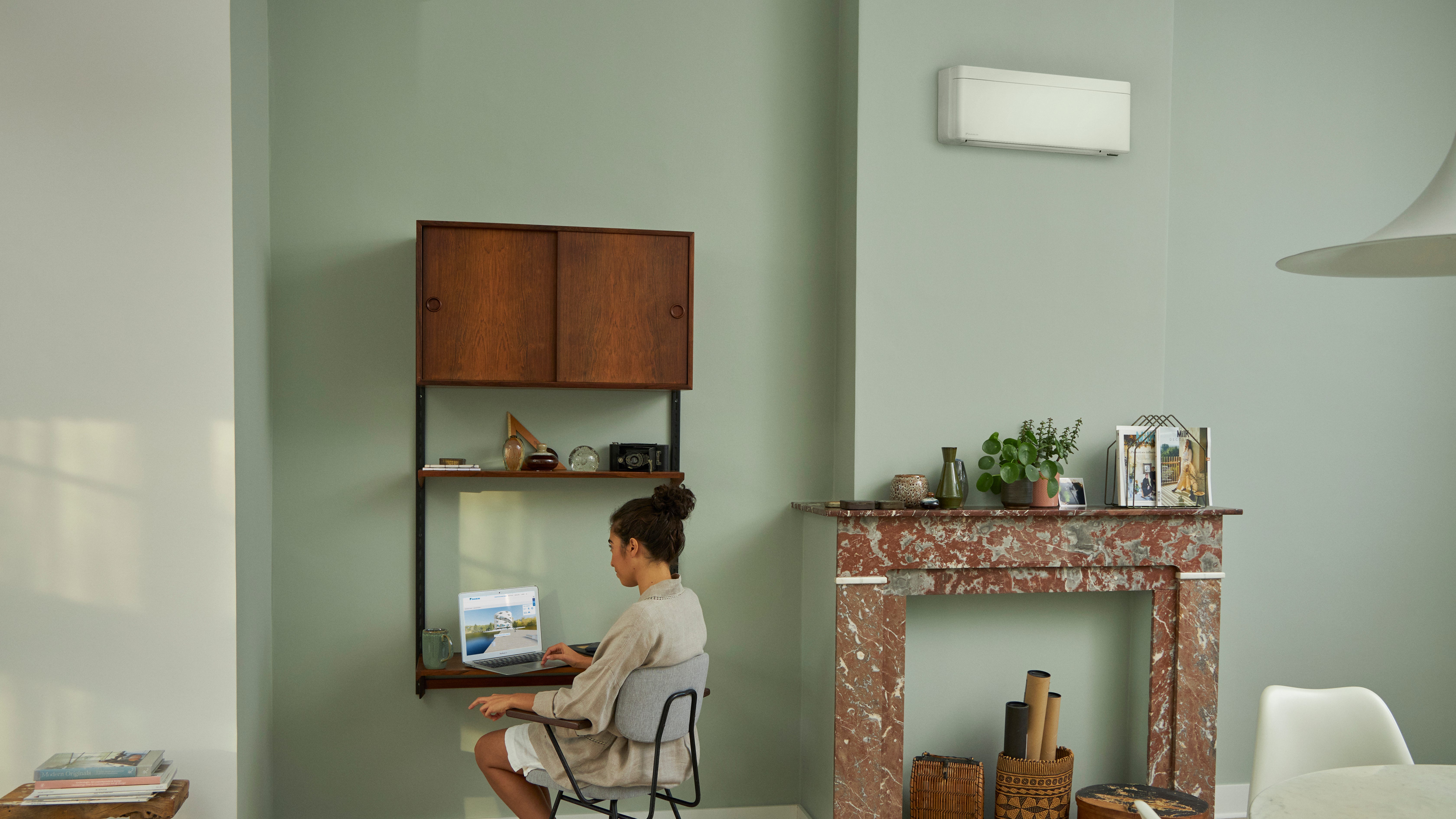 Vrouw bezoekt de Virtuele Showroom van Daikin vanaf haar laptop terwijl ze in haar mooie woonkamer aan haar tafel zit